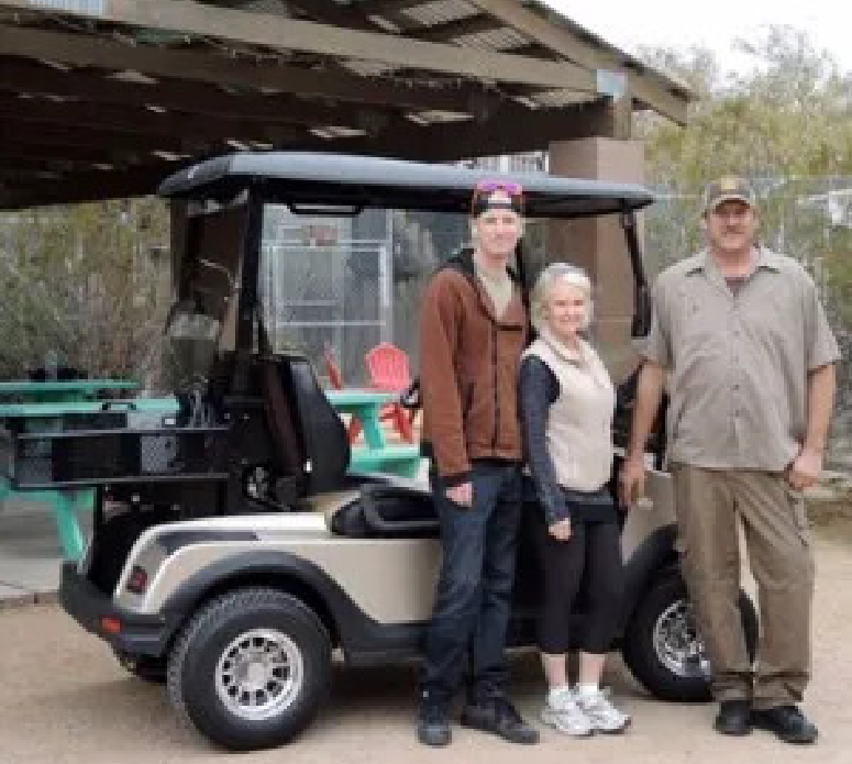 Three people standing in front of a golf cart.